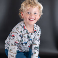 Smiling boy wearing soft monster truck and tree print raglan henley with buttoned front placket for active comfort.