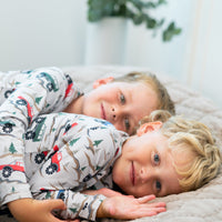 Two smiling boys lying on a bed wearing long sleeve henleys with a trucks and trees print, showcasing soft, comfortable button-up style for active play.