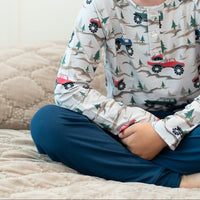 Child wearing soft raglan henley with monster truck and pine tree print, featuring buttoned front placket for comfortable active wear.