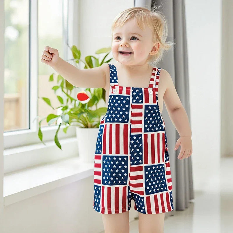 Toddler boy wearing patriotic baby overalls with American flag pattern standing and smiling indoors