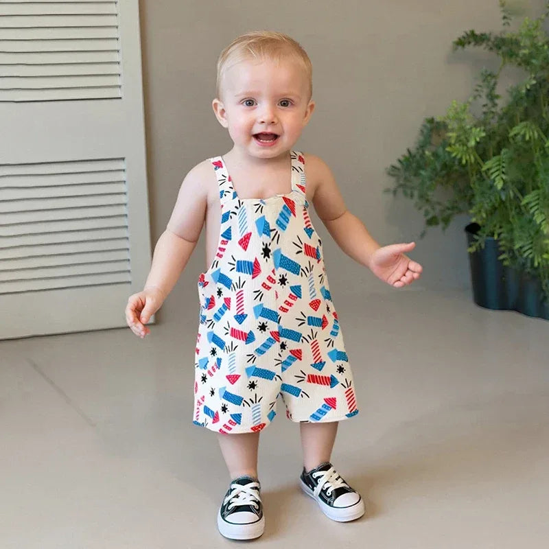 toddler boy wearing patriotic baby overalls with red white and blue fireworks print standing indoors