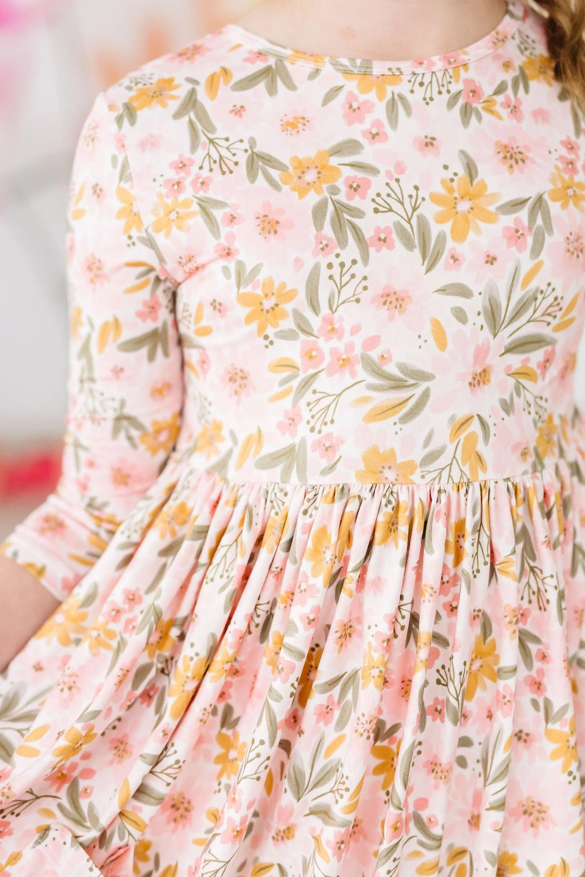 girl wearing peach floral girls twirl dress with 3/4 sleeves holding skirt gently