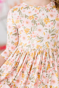 girl wearing peach floral girls twirl dress with 3/4 sleeves holding skirt gently