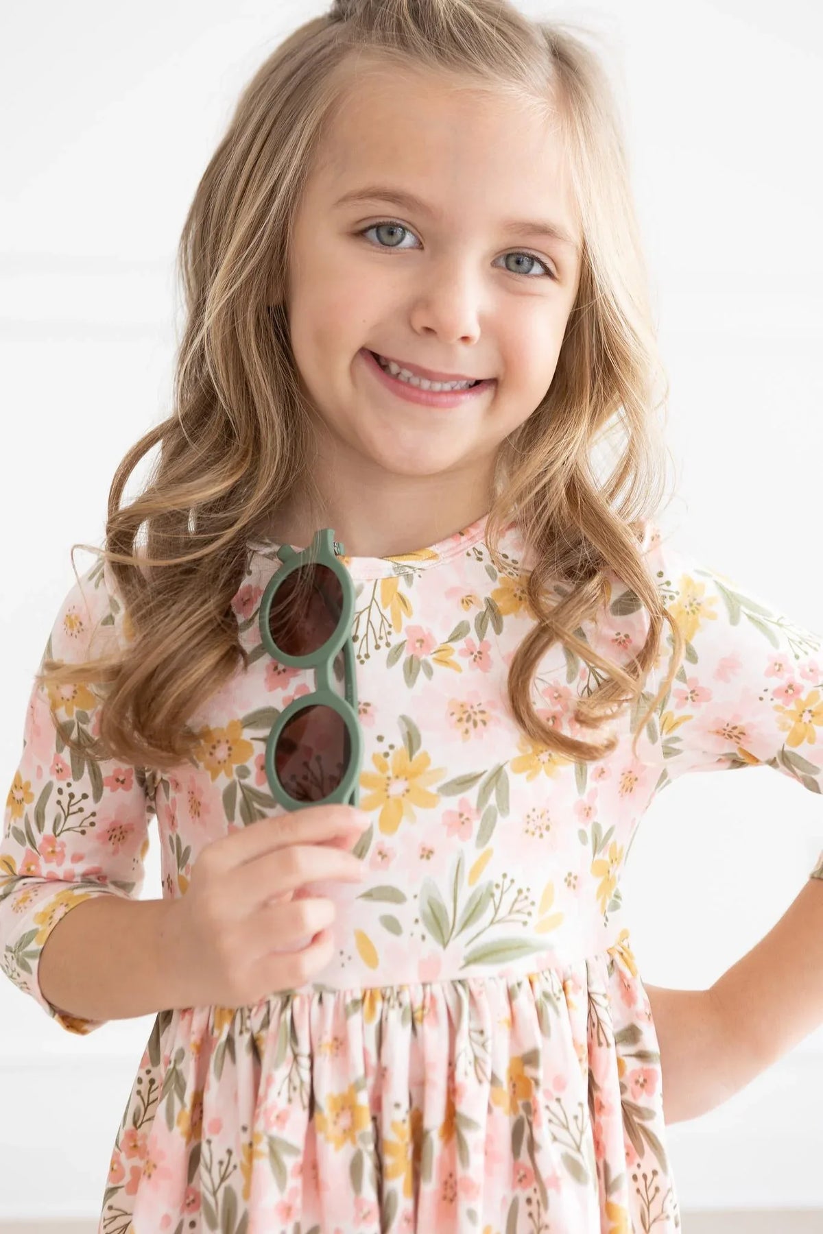 young girl wearing peach floral girls twirl dress holding green sunglasses smiling
