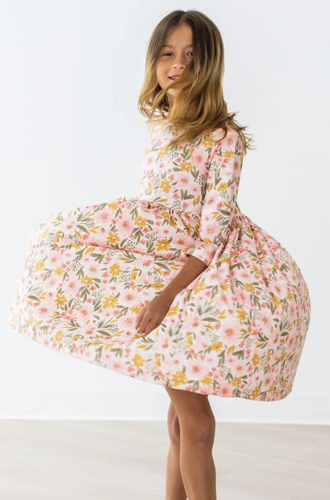 Girl wearing peach floral girls twirl dress by Mila & Rose twirling with dress flared out