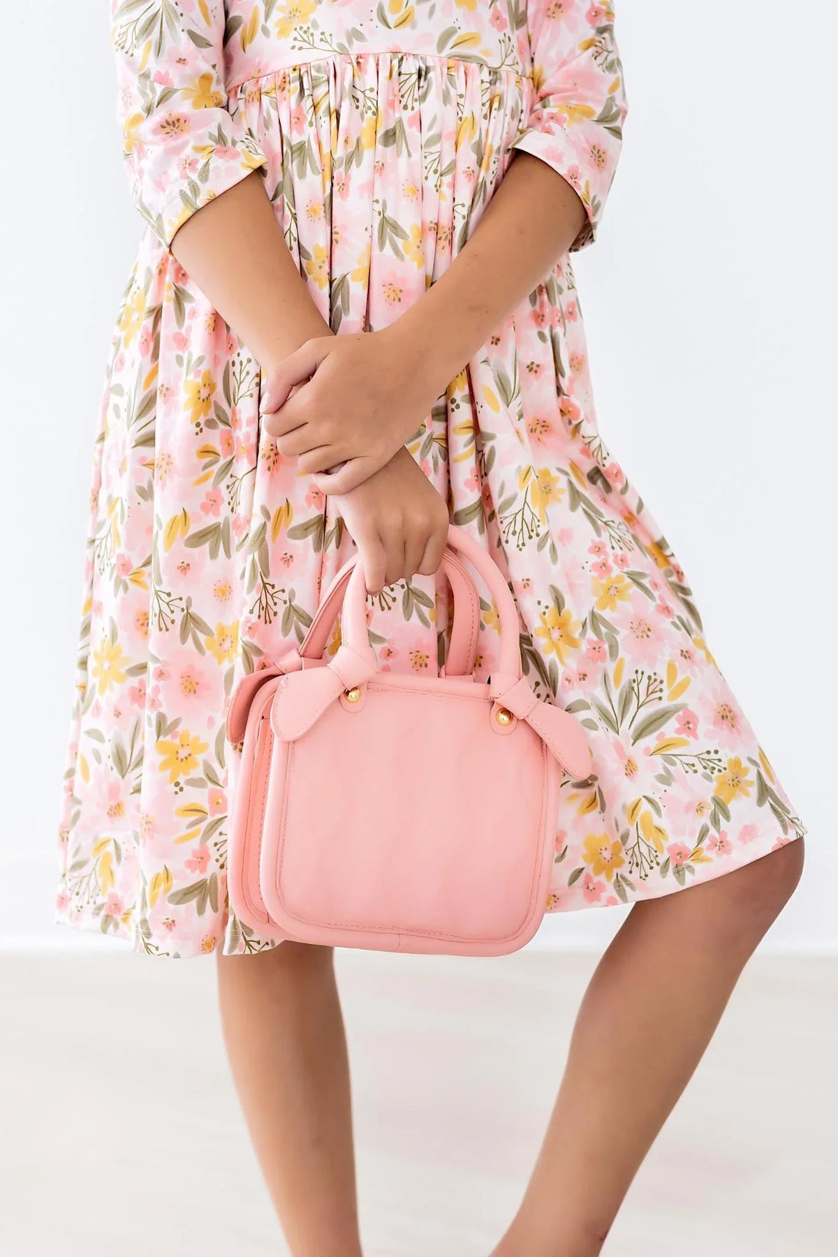 girl wearing peach floral girls twirl dress holding pink handbag with 3/4 sleeves