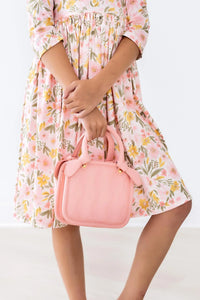 girl wearing peach floral girls twirl dress holding pink handbag with 3/4 sleeves