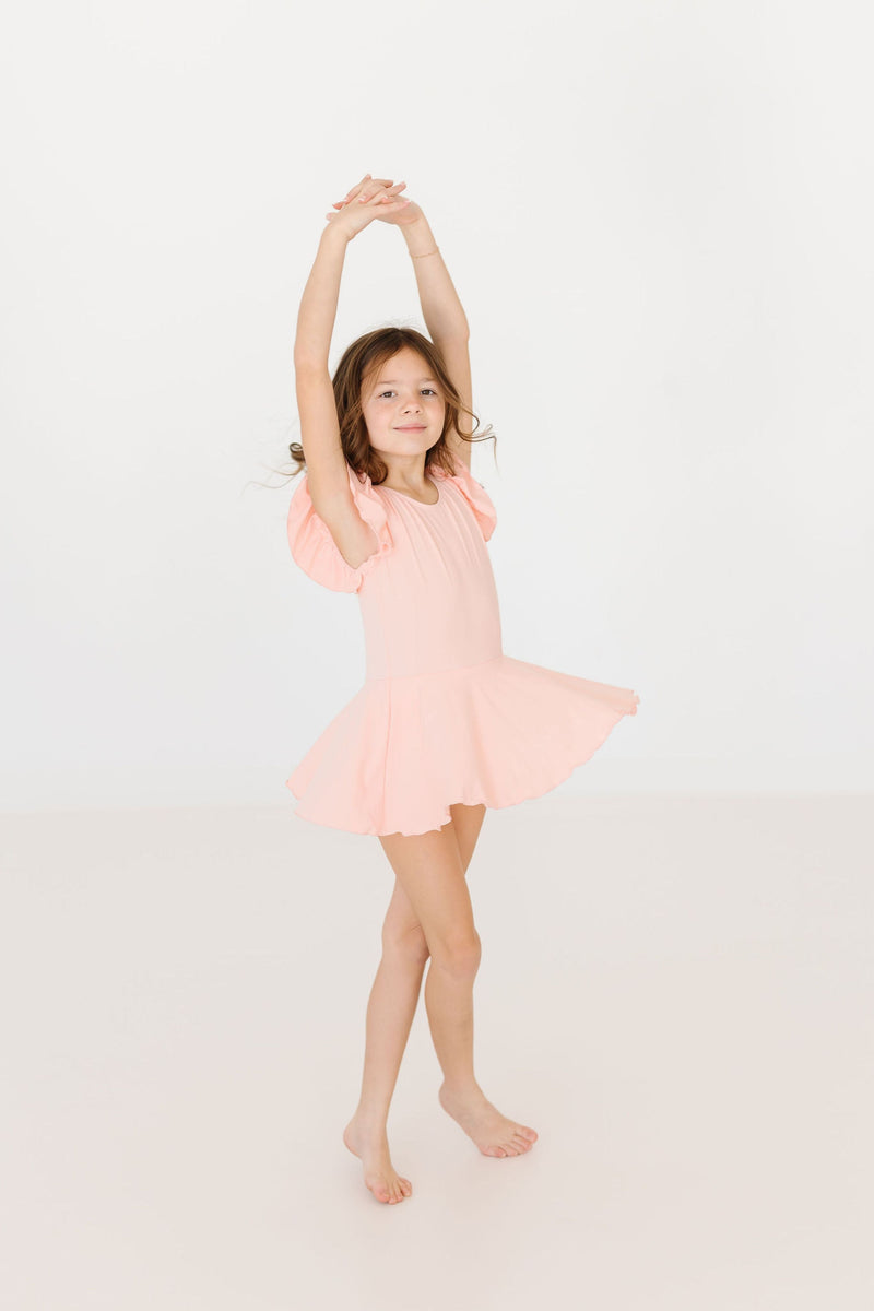 Child joyfully dancing in the Peach S/S Twirl Leotard by Mila & Rose, showcasing the fun design and vibrant peach color fit for a budding ballerina.