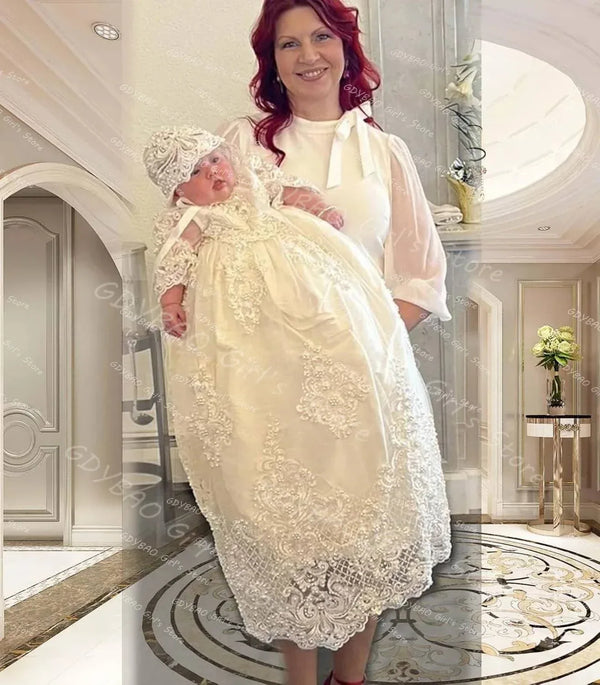 woman holding baby wearing white pearl lace christening gown and matching bonnet in elegant room