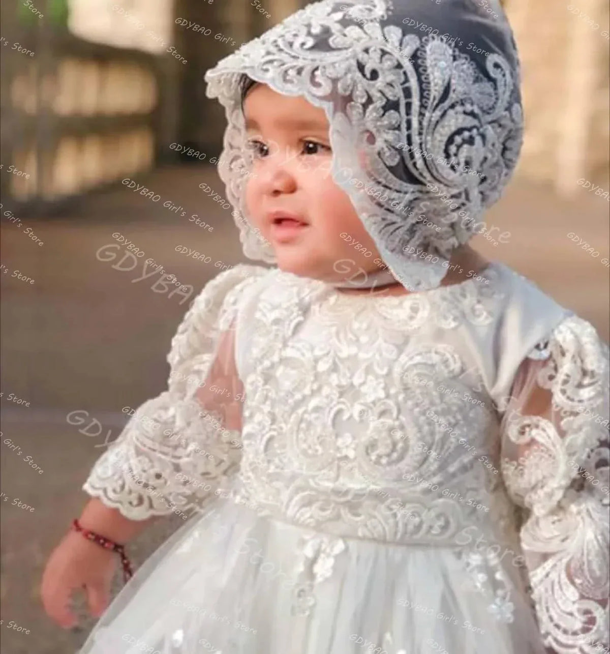 baby wearing white pearl lace christening gown with matching lace bonnet sitting outdoors
