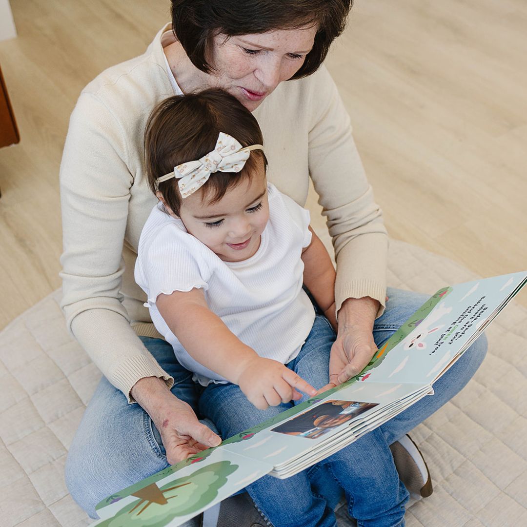 Peek a photo interactive book with toddler girl in white shirt and headband reading with grandmother