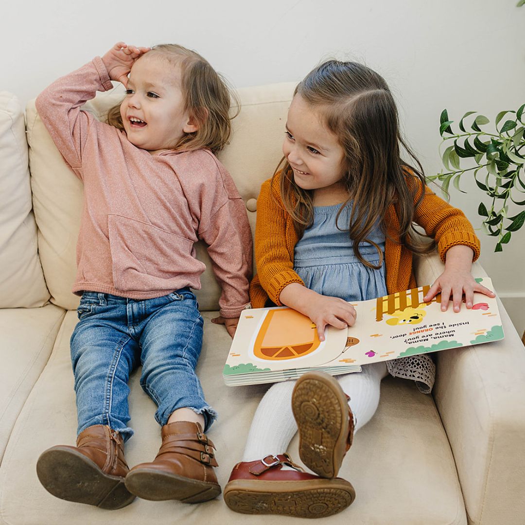 two young girls sitting on couch with peek a photo interactive book colorful pages toddler age