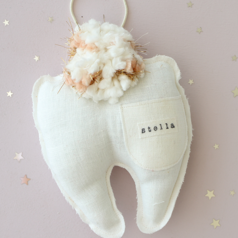 White plush toy shaped like a tooth with floral top on a light pink background