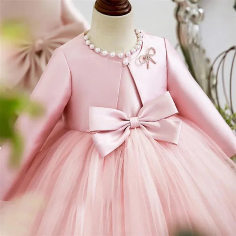 pink baptism dress for girls with long sleeve satin jacket, pearl necklace, and large bow detail