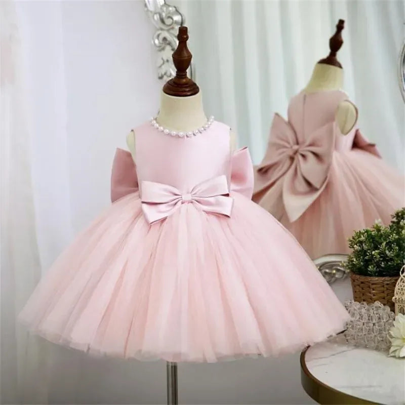 pink baptism dress for girls with sleeveless bodice, pearl neckline, and large bow detail