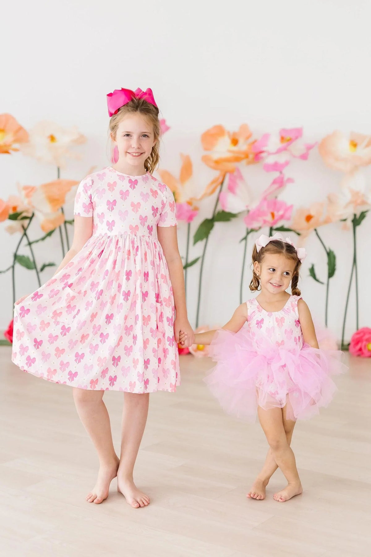Girls pink bow print tutu leotard for girls with tank top style worn by toddler, standing next to girl in bow print dress