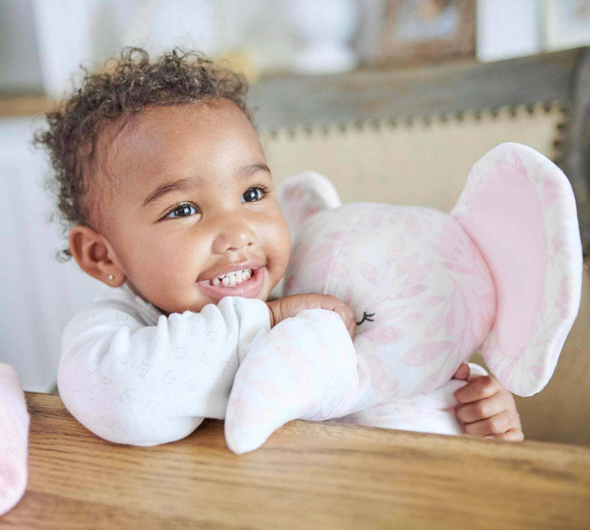 Pink elephant plush toy for infants with printed floral pattern held by smiling toddler