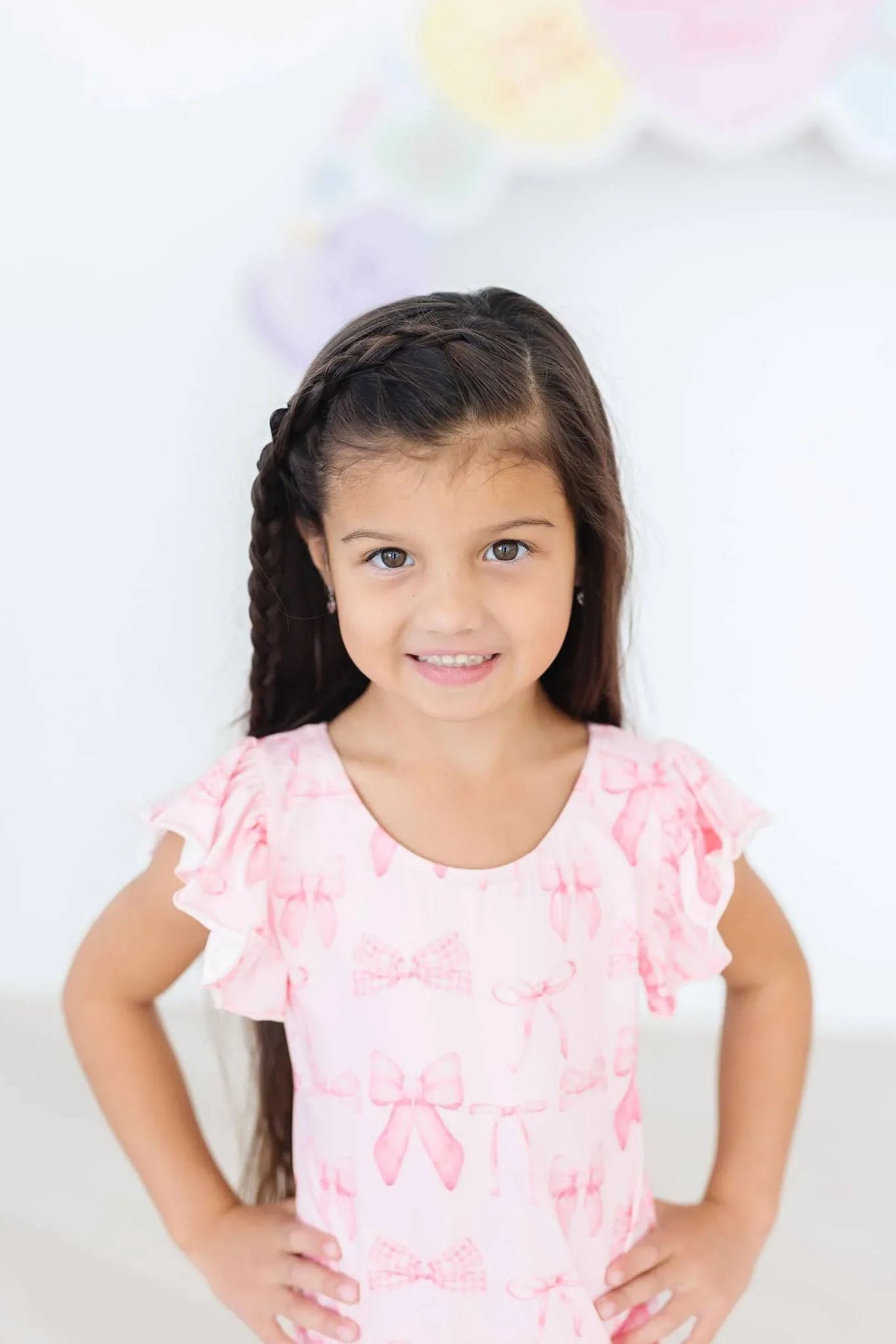 Toddler girl wearing pink flutter sleeve baby leotard standing with hands on hips smiling