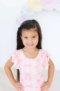 Toddler girl wearing pink flutter sleeve baby leotard standing with hands on hips smiling