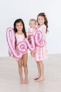 Toddler girl wearing pink flutter sleeve baby leotard holding pink love balloon with two girls