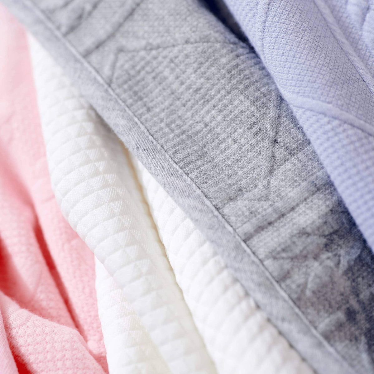 Close-up of pink knit baby blanket folded with white and gray blankets for newborns