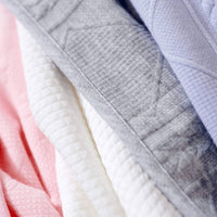 Close-up of pink knit baby blanket folded with white and gray blankets for newborns