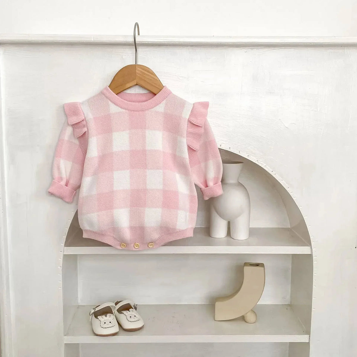 pink plaid baby romper for infants hanging on wooden hanger with puff sleeves and ruffle details