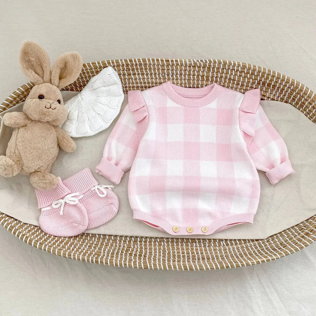 pink plaid baby romper with ruffle sleeves laid flat next to pink booties and a brown stuffed bunny