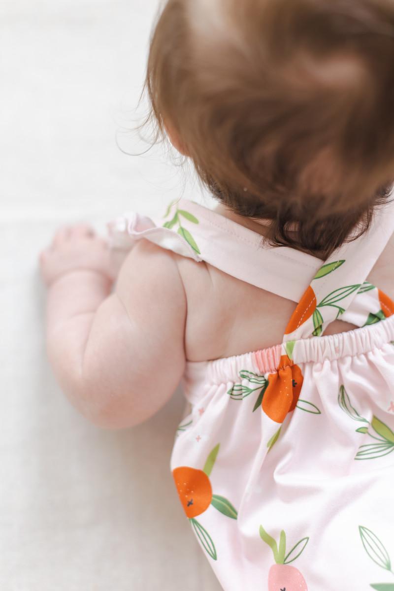 Baby wearing pink romper ruffle with orange fruit print and cross back straps