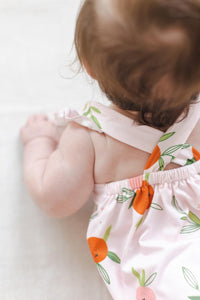 Baby wearing pink romper ruffle with orange fruit print and cross back straps