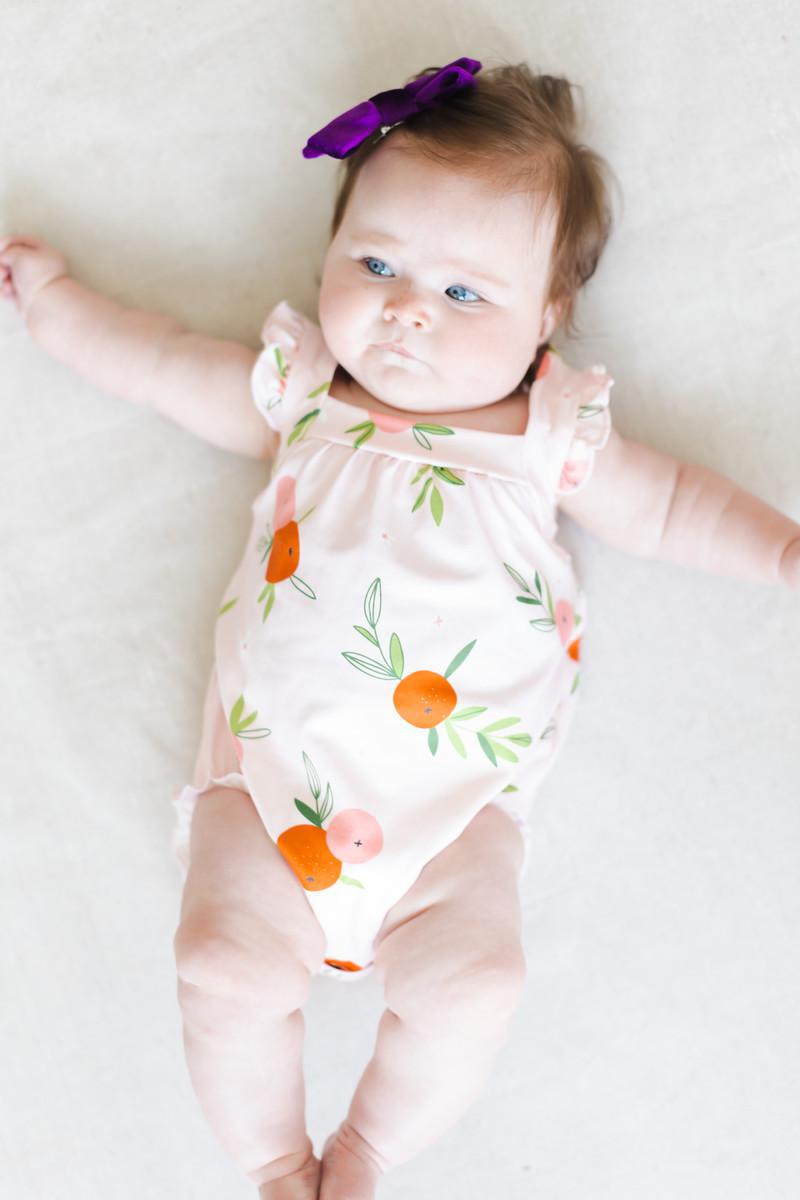 Baby girl wearing pink romper ruffle with orange fruit print and cross back design