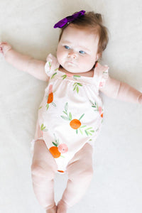 Baby girl wearing pink romper ruffle with orange fruit print and cross back design