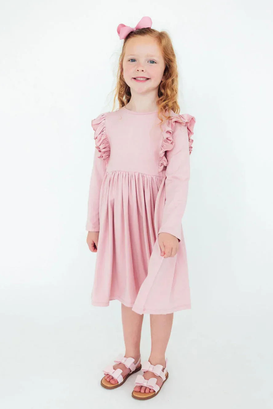 young girl wearing pink ruffle twirl dress for girls standing and smiling with matching pink bow