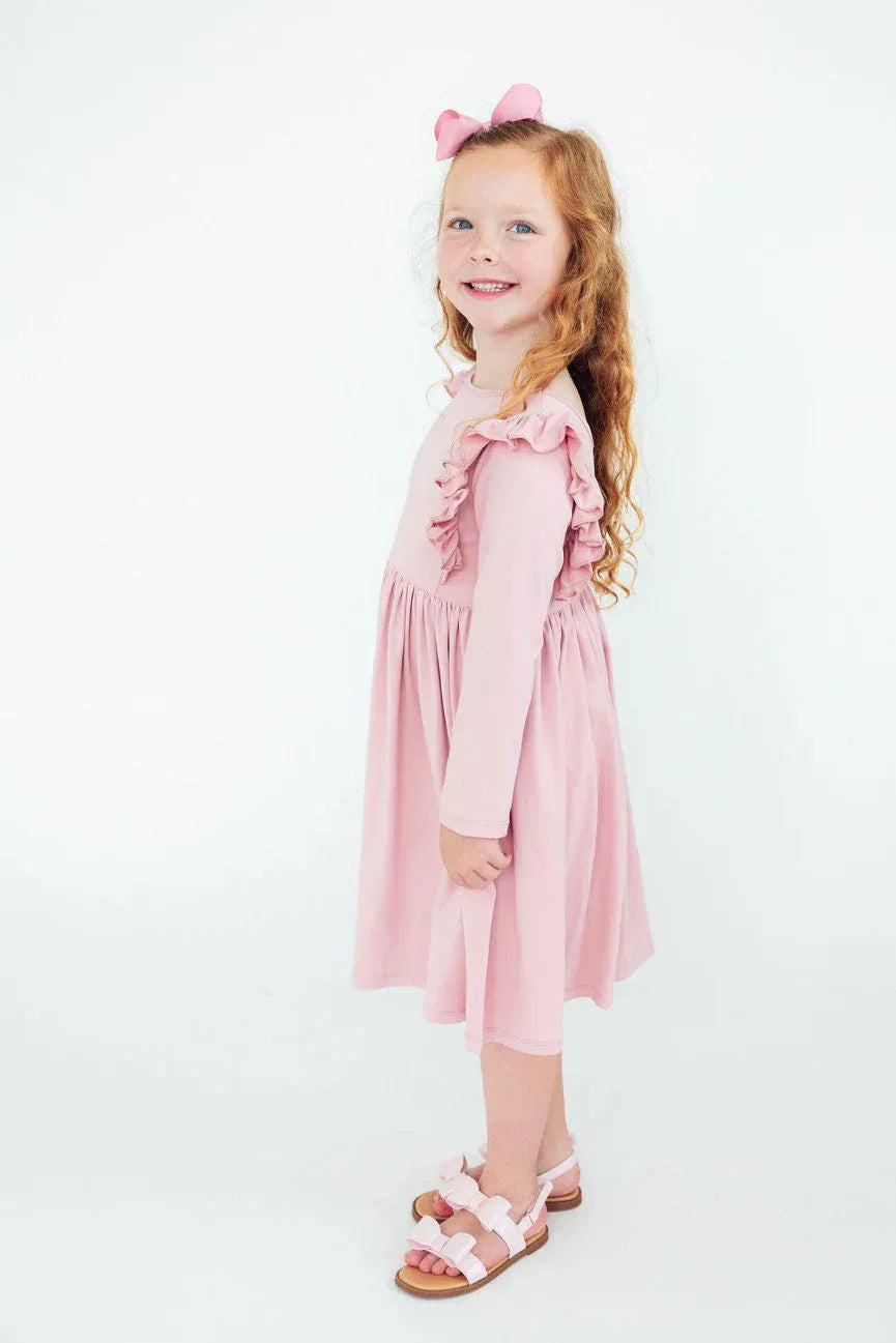 Young girl wearing pink ruffle twirl dress for girls standing and smiling with bow in hair