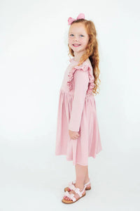 Young girl wearing pink ruffle twirl dress for girls standing and smiling with bow in hair