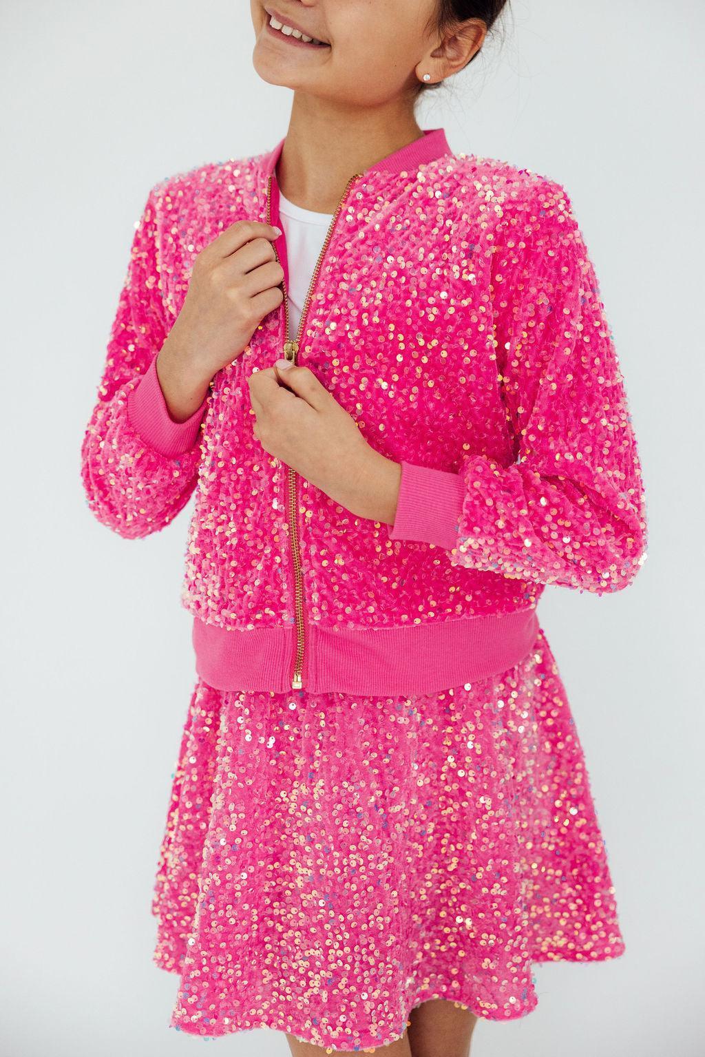 Girl wearing a pink sequin jacket for girls zipped up over a matching pink sequin skirt