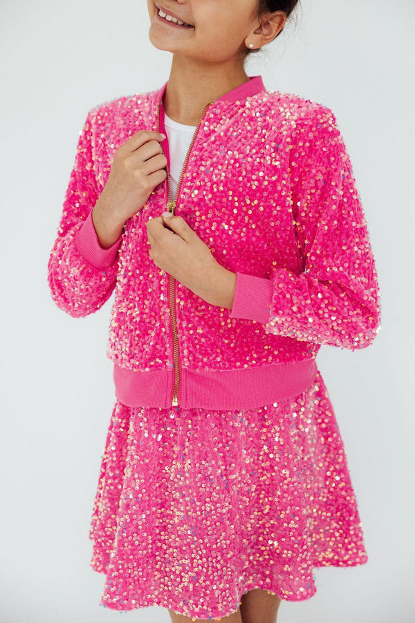 Girl wearing a pink sequin jacket for girls zipped up over a matching pink sequin skirt