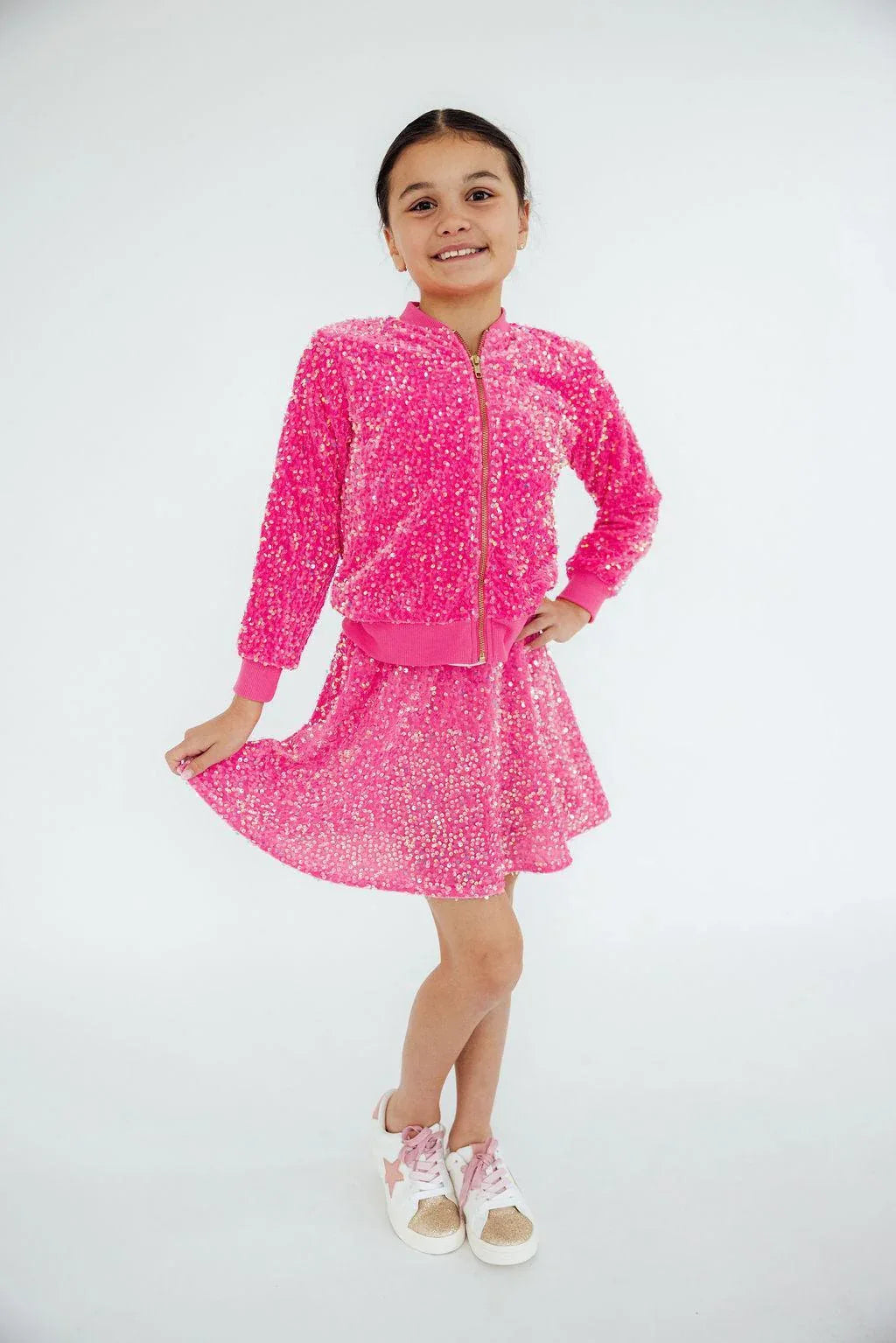 Girl wearing pink sequin jacket for girls standing and holding her skirt while smiling