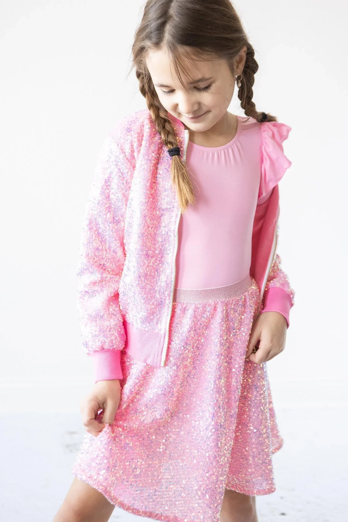 Young girl wearing pink sequin jacket for girls and matching skirt, looking down and smiling