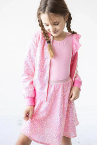 Young girl wearing pink sequin jacket for girls and matching skirt, looking down and smiling
