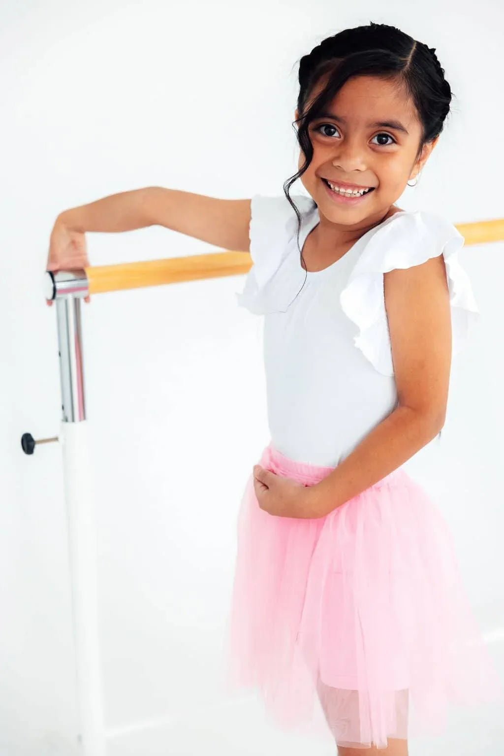 young girl wearing pink tutu shorts for girls smiling and posing at ballet barre