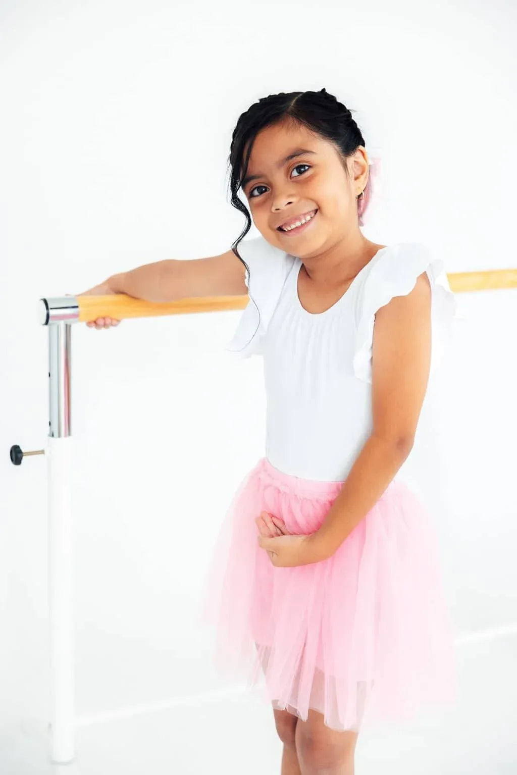Young girl wearing pink tutu shorts for girls standing and holding ballet barre smiling