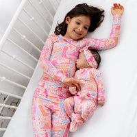 Girl in The Second-Skin 2-Piece Long Sleeve Pajama Saddle Up cowgirl print, pink pastel, smiling on white surface.