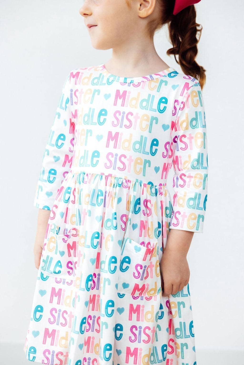 young girl wearing white pocket twirl dress with colorful middle sister print and 3/4 sleeves