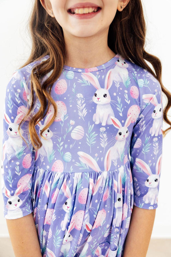 young girl wearing a purple pocket twirl dress with bunny and egg print smiling