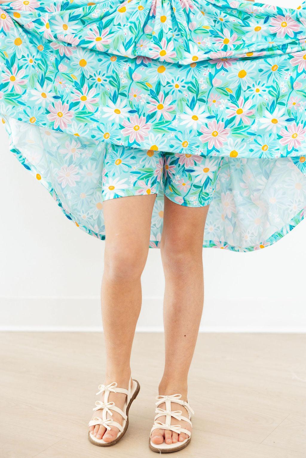 Girl wearing Mila & Rose preppy daisy twirl dress for girls in blue with white daisies and green leaves