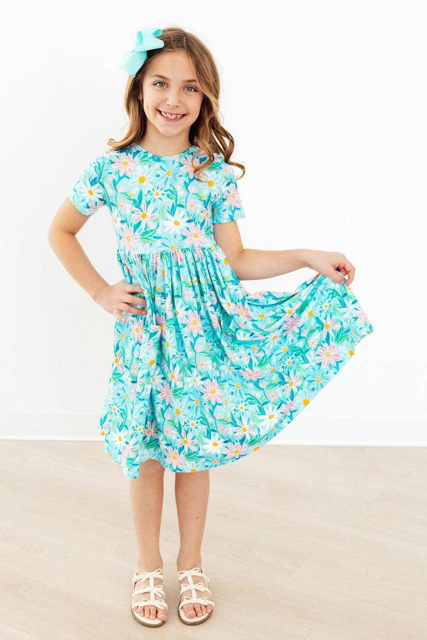 Young girl wearing a blue preppy daisy twirl dress for girls holding the skirt out