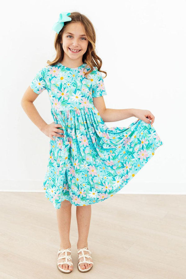 Young girl wearing a blue preppy daisy twirl dress for girls holding the skirt out