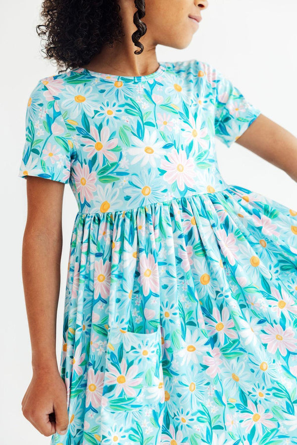 Girl wearing preppy daisy twirl dress for girls in blue holding the skirt and twirling
