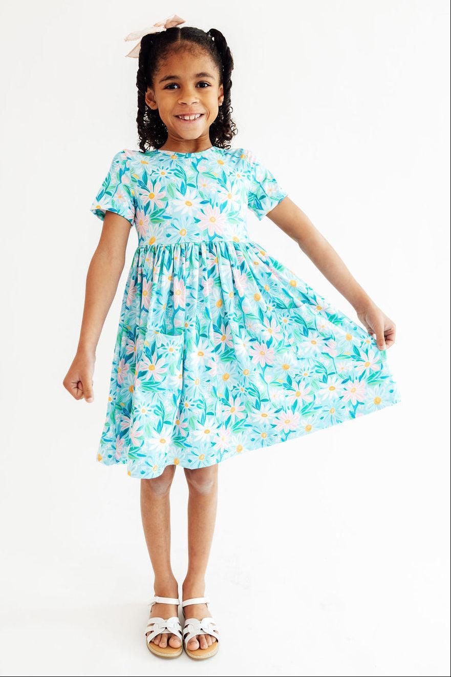 Girl wearing blue preppy daisy twirl dress for girls holding skirt out in a playful pose